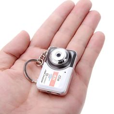 a hand holding a small camera keychain in it's left hand,