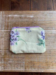 a small purse sitting on top of a wooden table covered in purple flowers and leaves