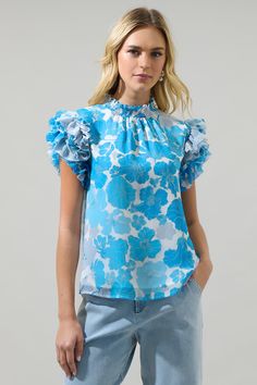 The Kerela Floral Brenna Mock Neck Ruffle Blouse is the perfect piece to add to on-the-go outfit. Ruffle layered short sleeves frame a ruffled high neckline. The blouse features a little shirring along the neckline and maintains a straight fit. Wear it with white pants and matching shoes. - Mock neck- Ruffle layer sleeves- Keyhole- Classic fit- Color: White Blue ComboSize + Fit - Model is 5'8" and wearing size XS- Measurements taken from size S - Chest: 38 1/2"- Length: 24" Fabric Self: 100% Pol Blue Flutter Sleeve Tops With Ruffle Hem, Blue Floral Print Tops With Ruffle Sleeves, Blue Tops With Ruffle Hem And Flutter Sleeve, Blue Floral Print Ruffle Sleeve Blouse, Blue Floral Print Blouse With Ruffle Sleeves, Blue Ruffle Sleeve Blouse With Floral Print, Light Blue Ruffled Blouse For Spring, Spring Light Blue Ruffled Blouse, Light Blue Ruffled Short Sleeve Tops