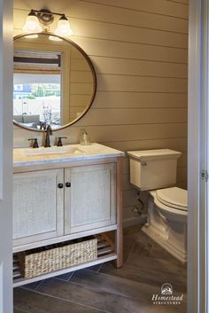 a white toilet sitting next to a bathroom sink under a round mirror in a bathroom