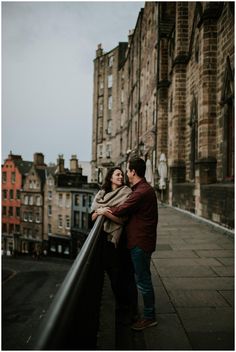 a man and woman standing on top of a building next to each other with buildings in the background