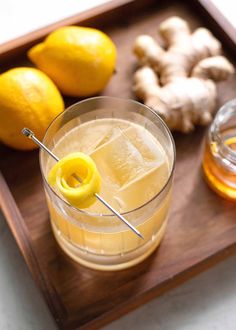 a close up of a drink in a glass on a tray with lemons and ginger