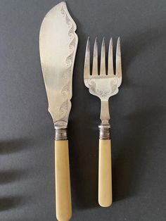 two forks and a knife sitting next to each other on top of a black surface