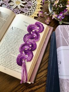 an open book sitting on top of a wooden table next to purple crocheted flowers