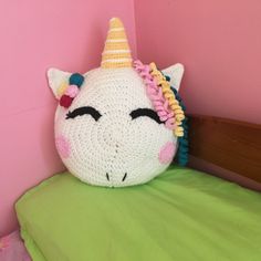 a crocheted stuffed unicorn head sitting on top of a green pillow in a pink room