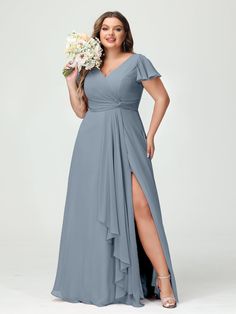 a woman in a long grey dress holding a bouquet and posing for the camera with her hands on her hips