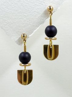 These earrings are sleek and modern, crafted from golden brass and semi precious stone.  The matte, black onyx stone features among the geometric shapes, an elongated semi-circle, layered with a solid brass oval hangs below, adding a touch of contrast and sophistication to the overall design.  The combination of geometric shapes, the matte black stone, and the metallic shine creates an elegant, minimalist aesthetic. A brass ball stud with stainless steel post holds the design from the top.  Approximate measurements- 4.5cms long 1.5cms wide All Set Theory jewellery comes with care instructions and a polishing pad to keep your jewellery looking shiny and fabulous! ✨ Modern Gold Onyx Jewelry, Modernist Black Earrings For Gift, Modernist Black Earrings As Gift, Minimalist Black Linear Drop Earrings, Modern Matte Gold Metal Earrings, Black Minimalist Metal Earrings, Minimalist Black Drop Earrings, Modern Black Geometric Earrings, Matte Gold Minimalist Metal Earrings