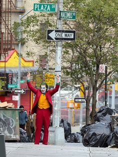 a man dressed as the joker standing next to a street sign