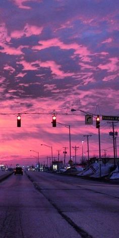 the sky is pink and purple as cars drive down an empty street at night time