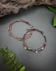 two bracelets with beads and stones on a table next to some green leafy branches