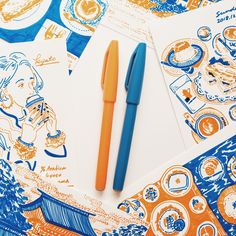 an orange and blue pen sitting on top of a piece of paper next to some drawings