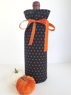 an orange and black polka dot wine bottle cover next to a pumpkin on a white table