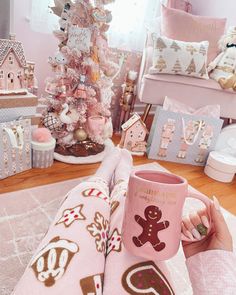 a person holding a pink coffee mug in front of a christmas tree with gingerbreads on it