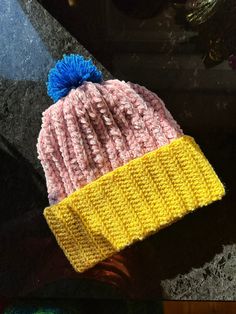 a yellow and pink knitted hat with blue pom - pom on top