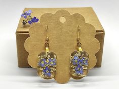 a pair of earrings with blue and yellow flowers on them sitting in a cardboard box