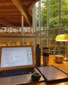 an open laptop computer sitting on top of a wooden desk next to a cup and lamp