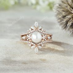 a close up of a ring with pearls and diamonds on the surface next to a pine cone