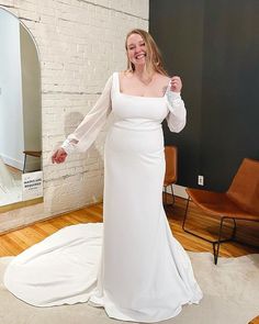 a woman standing in front of a mirror wearing a white dress and posing for the camera