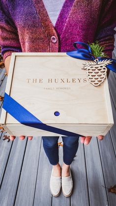 a person holding a wooden box with a pineapple on it and blue ribbon around the bottom