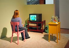 a woman sitting in front of a television on top of a wooden table next to a fish bowl