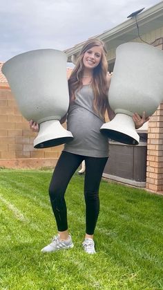 a pregnant woman is holding two large white objects in her hands while standing on the grass