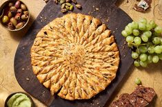 a pie sitting on top of a wooden cutting board next to grapes and crackers