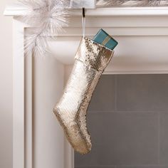 a gold christmas stocking hanging from a mantel with silver feathers on it's top