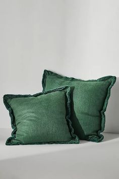 two green pillows with ruffled edges on a white bed side by side in front of a plain wall