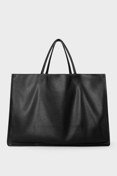 An extra-large black tote bag with a square body. It has an open top with two magnetic closures. The bag has 2 handles to be carried handheld or as a shoulder bag. Minimalist Tote Bag With Smooth Grain, Minimalist Smooth Grain Tote Bag, Minimalist Smooth Grain Shoulder Bag For Shopping, Minimalist Smooth Grain Tote Shoulder Bag, Minimalist Rectangular Shoulder Bag With Rolled Handles, Minimalist Smooth Grain Top Handle Bag, Sleek Textured Leather Tote Bag, Minimalist Structured Bag With Top Carry Handle, Minimalist Structured Bags With Top Carry Handle