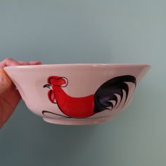 a hand holding a bowl with a rooster painted on it