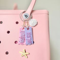 a pink purse with two tags attached to the handle and starfish charms hanging from it