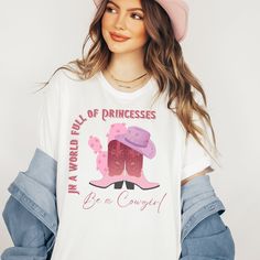 "Looking for a vintage western cowgirl t-shirt that will make you say \"In a world full of princesses, be a cowgirl!\" Look no further than this oversized comfort colors tee. Perfect as a western shirt, t-shirt dress, or cowgirl t-shirt, this tee features a bold western graphic that is sure to turn heads. With its vintage style and classic cowgirl shirt design, this tee is a must-have for any cowgirl looking to add some Shania flair to their wardrobe. So what are you waiting for? Saddle up and grab your own cowgirl tee today! See my shop for other options.  Click link below. https://www.etsy.com/shop/StaySmartDesign?ref=seller-platform-mcnav *Comfort color garment dyed shirts are super popular right now and these cotton washed tees are the nicest, softest shirts to wear. The colors are tru Spring Letter Print T-shirt For Rodeo, Relaxed Fit Western T-shirt For Ranch, Western Style Relaxed Fit T-shirt For Ranch, Western Style T-shirt For Ranch In Summer, Western Style Summer T-shirt, Oversized Tops For Rodeo In Spring, Oversized Spring Tops For Rodeo, Graphic Tee For Western-themed Spring Events, Spring Graphic Tee For Western-themed Events