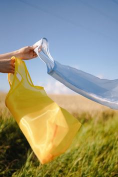 a person holding a plastic bag in their hand while walking through the grass on a sunny day