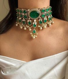 Inspired by the opulent designs of Sabyasachi, this emerald green Victorian choker set is the epitome of elegance and timeless beauty. The choker, meticulously crafted, features a central emerald stone surrounded by intricate gold filigree work that echoes the grandeur of the Victorian era. Each detail is a testament to the exquisite craftsmanship, with tiny pearls and delicate gold beads enhancing the necklace's regal appeal. Complementing the choker are a pair of matching earrings that mirror Indian Choker Necklace Set, Victorian Choker, Unique Wedding Jewelry, Indian Choker, Indian Choker Necklace, Neck Pieces Jewelry, Sabyasachi Jewellery, Pearl Jewelry Design, Indian Jewelry Sets