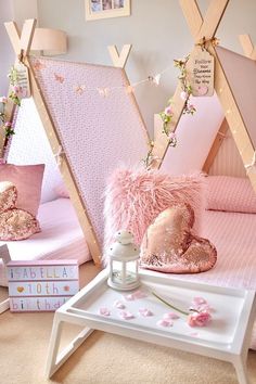 a room with pink and gold decor on the walls, bedding and pillows in front of two teepee tents