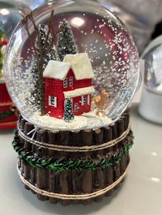 a snow globe with a red house in the center and trees inside it on top of a table