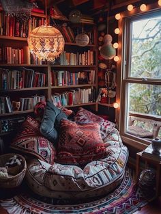 a living room filled with lots of books and furniture next to a large window covered in lights