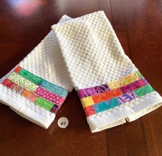 two white towels are sitting on a wooden table and one is folded up with different colored strips