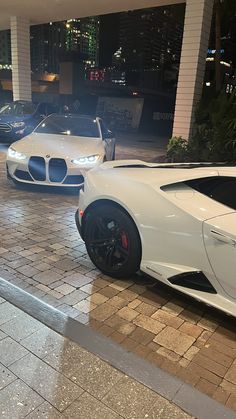 two white sports cars parked next to each other in front of a building at night