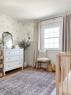 a baby's room with white furniture and floral wallpaper, along with a large rug on the floor