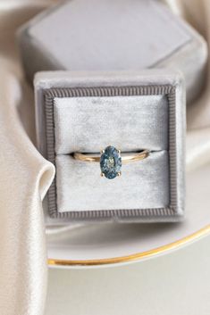 an engagement ring with a blue topaz sits in a velvet box on a table