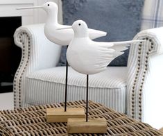 two white birds standing on top of wooden blocks in front of a couch and chair