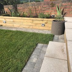 a wooden planter sitting on top of a lush green grass covered field next to a brick wall