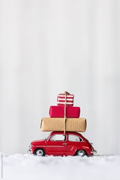 a small red car carrying presents on top of it's roof in the snow