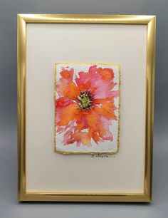 an orange and pink flower in a gold frame on a gray background with white border