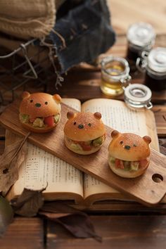 three small sandwiches are sitting on a wooden tray next to an open book and other items