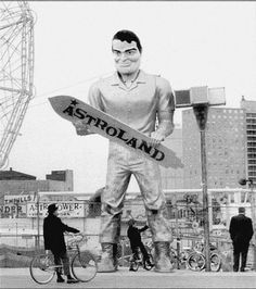 a black and white photo of a man holding a skateboard in front of a ferris wheel