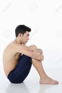 a shirtless man sitting on the floor with his legs crossed and looking off to the side