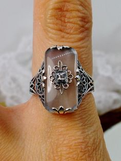 Frosted Camphor Glass Solid Sterling Silver Ring Grace Design#D233 This is a lovely antique Edwardian era inspired filigree ring. This gorgeous ring is created in stunning frosted camphor glass. The glass is embellished with a delicate floral filigree. The top of the ring holds a center set 1mm round cut gemstone (Choose from white Cubic Zirconia, lab created Moissanite, or Natural/Genuine White Diamond). The frosted glass is 18mm x 19mm. The ring sits 18mm north-south and 10mm east-west on the Art Deco Carved Rings For Wedding, Vintage Silver Ring With Intaglio, Art Deco Silver Ring With Intaglio, Vintage Silver Intaglio Rings, Elegant Etched Filigree Ring For Anniversary, Elegant Etched Filigree Anniversary Ring, Silver Art Deco Intaglio Ring, Vintage Carved Filigree Ring Gift, Carved Vintage Filigree Ring Gift