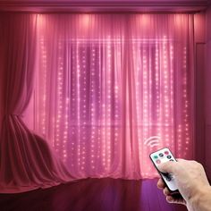 a person is holding a remote control in front of a curtain with lights on it